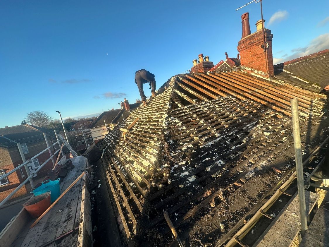 The old roof stripped back to the rafters, with a roofer clearing the last of it from the scaffold