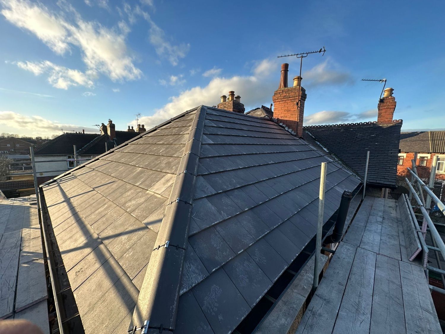The finished roof in dark grey slate-effect tiles, with neat hip tiles and the chimneys behind