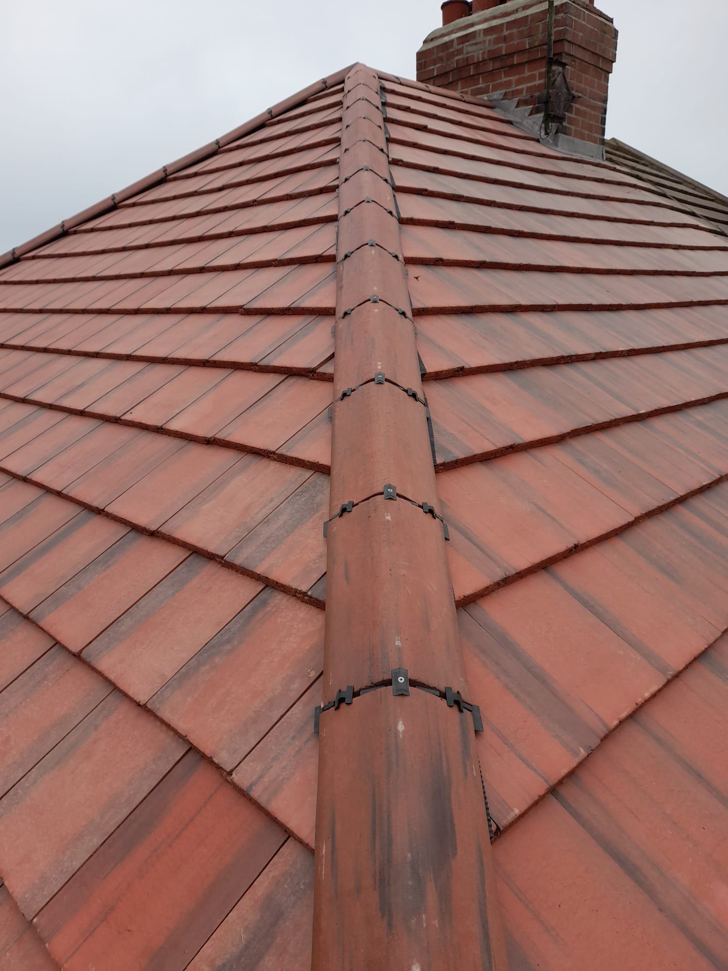 Red dry-fixed ridge running up a hipped plain-tile roof