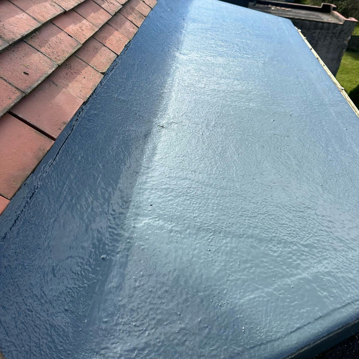 Freshly coated GRP flat roof beside red roof tiles