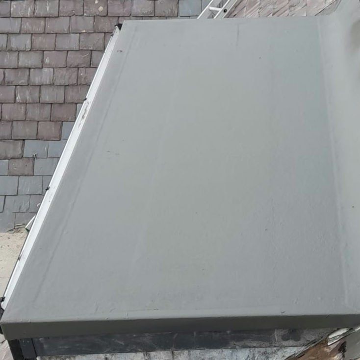 Grey GRP flat roof with trimmed edges beside a slate roof