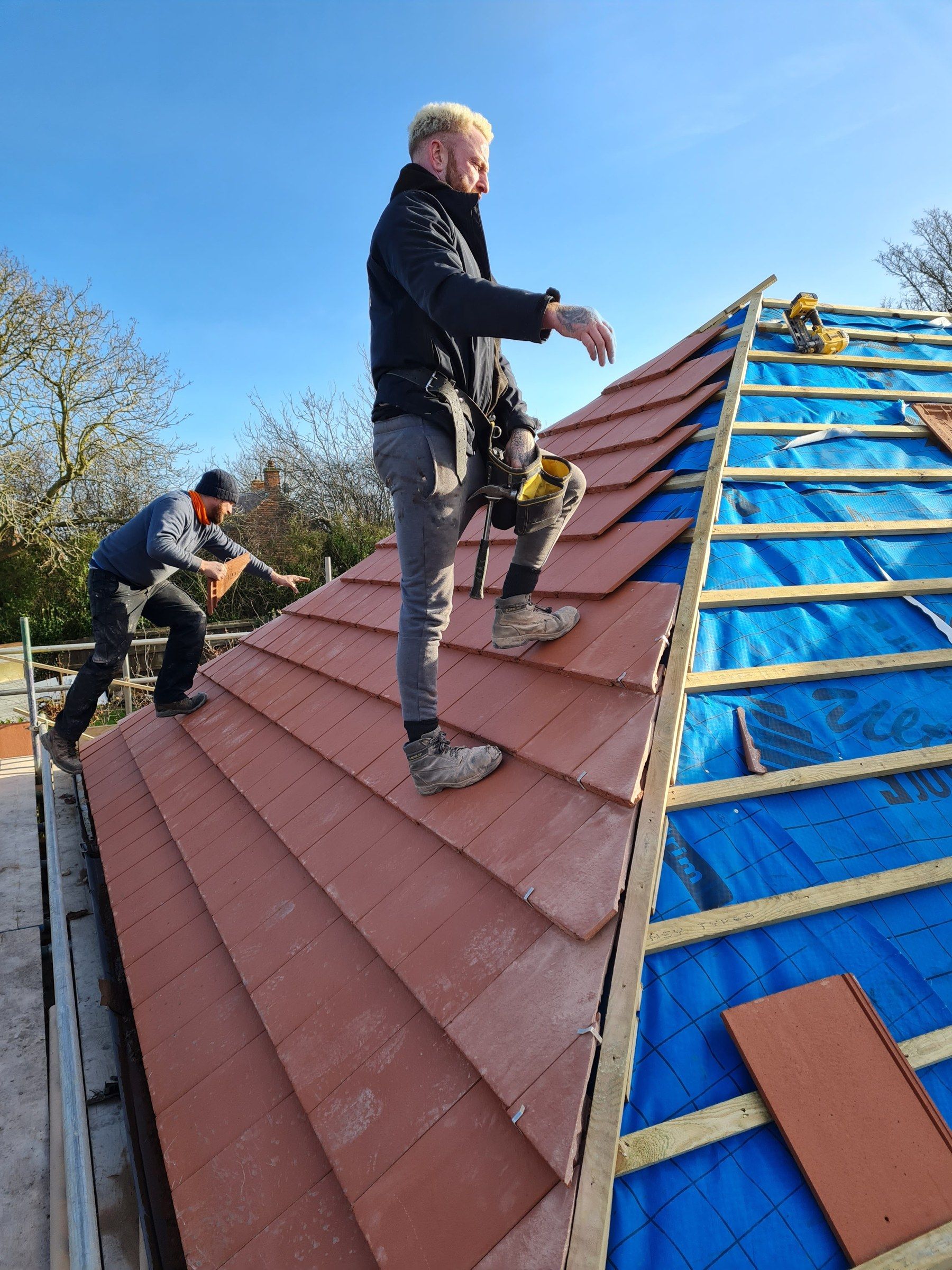 Two roofers laying new tiles over fresh battens and membrane