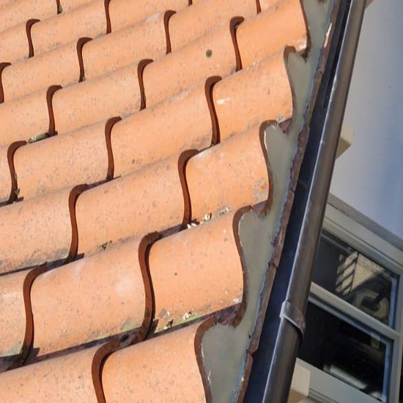 Clay pantiles at the eaves above a new black gutter