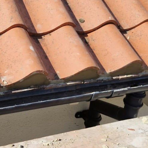 Clay pantiles at the eaves with a black gutter after repair
