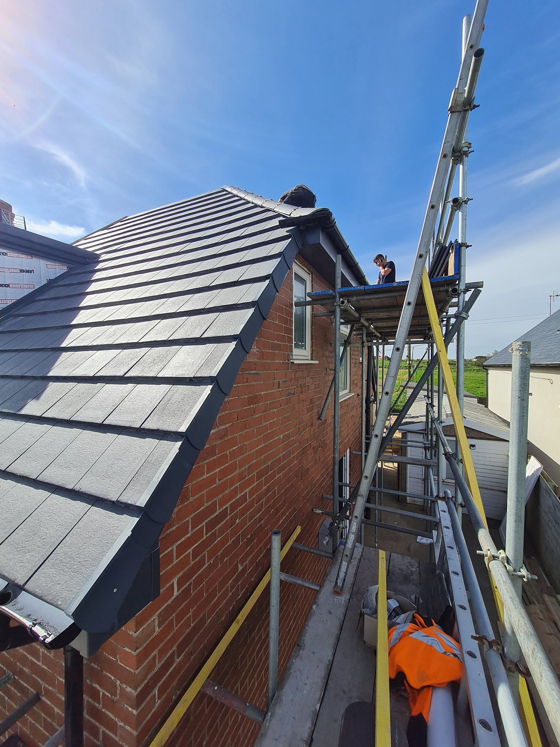 Gable end with new slate-effect tiles and dry verge, scaffold in place