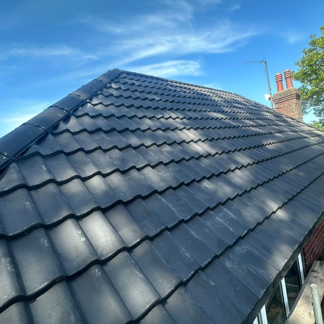 New dark grey interlocking tiles on a hipped roof in the sun