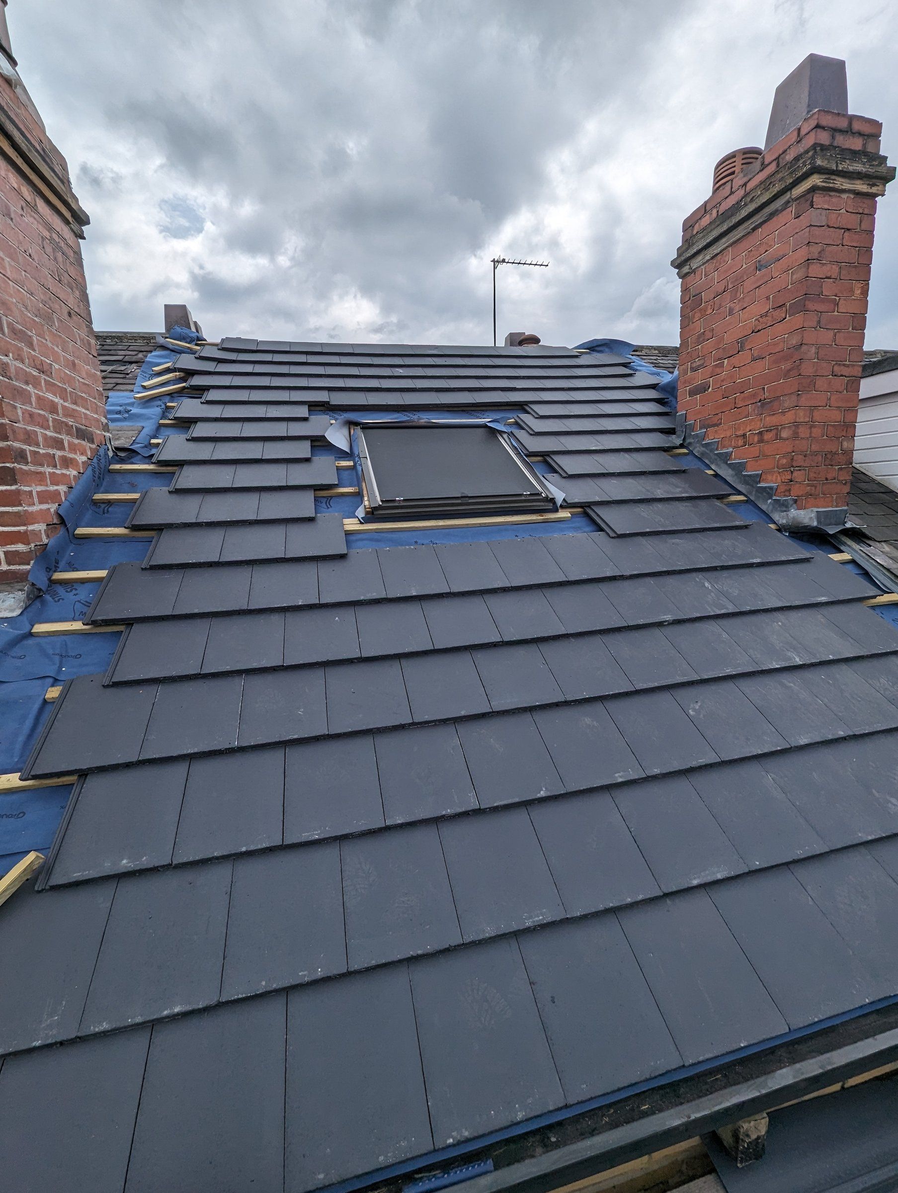 Slate re-roof in progress with a new roof window beside the chimney