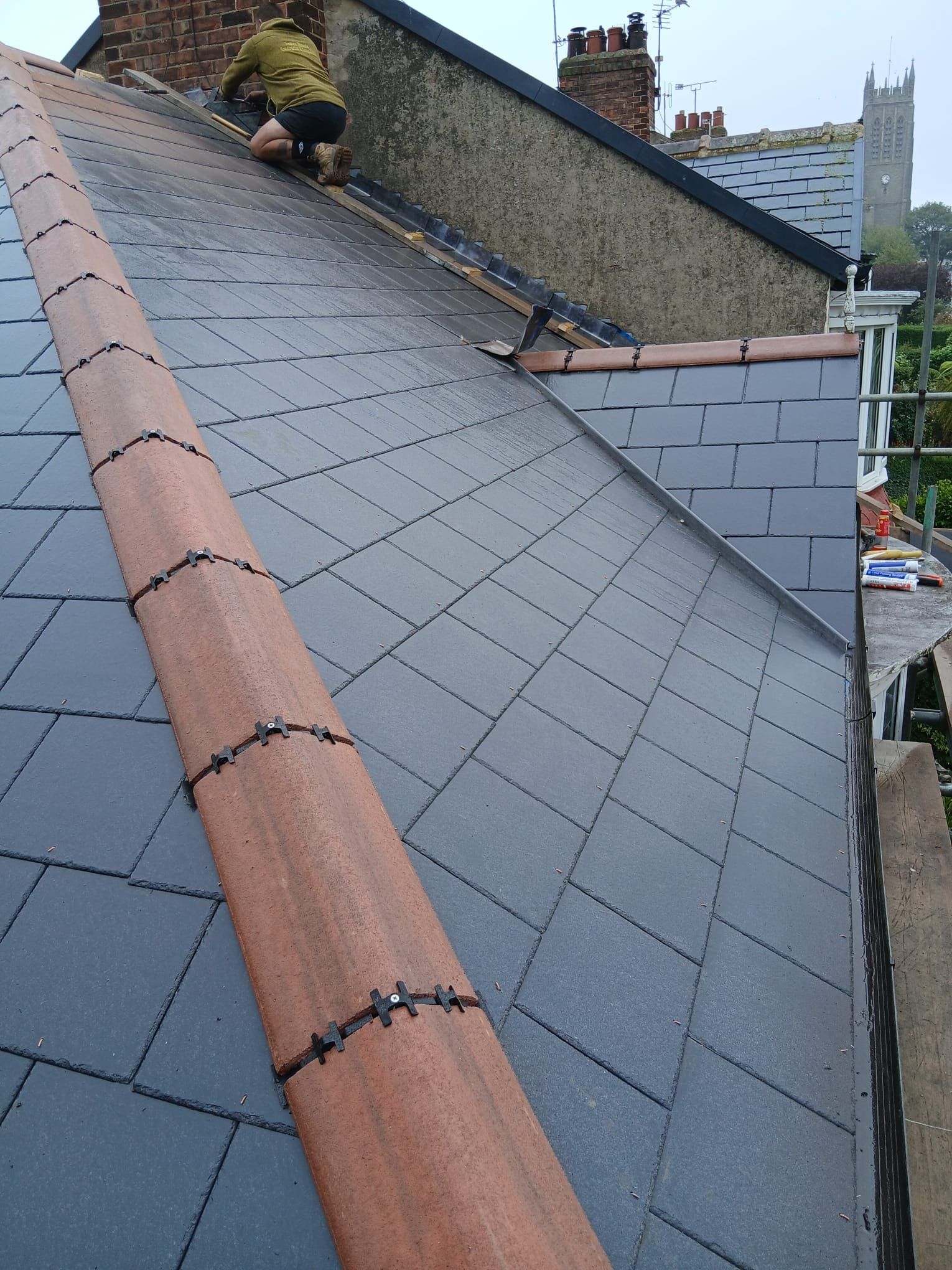 Slate roof with a red clay ridge and a roofer at the far end